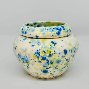 May include: A white ceramic planter with a blue and yellow speckled pattern. The planter has a removable top for easy planting.