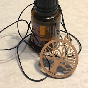 May include: A brown wooden tree of life pendant on a black cord with a small amber glass bottle of lavender essential oil.