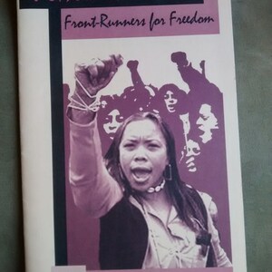 May include: Book cover with a purple image of a woman raising her fist in the air. The book title is "Women of Color: Front-Runners for Freedom" and the author is "Nancy Reiko Kato".