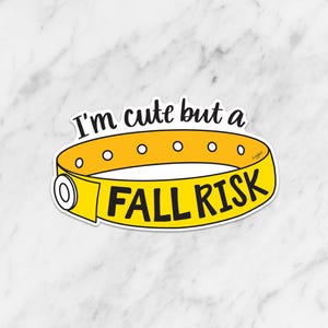 May include: A yellow sticker with the text "I'm cute but a FALL RISK" in black. The sticker is in the shape of a hospital wristband, with small white circles and a clasp detail. The background is a white marble pattern.