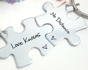 May include: Two silver puzzle pieces with key rings attached. The pieces fit together and have the words "Love Knows" and "No Distance" engraved on them.