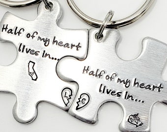 May include: Two silver puzzle piece keychains with the text "Half of my heart lives in..." on each piece. One piece has a California outline and the other has a heart with a broken line through it.