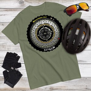 May include: A green t-shirt with a black and white graphic of a mountain bike wheel with the text "Mountain 24/7 MTBlife" printed on it. The graphic includes a chain, gears, and a brake rotor.