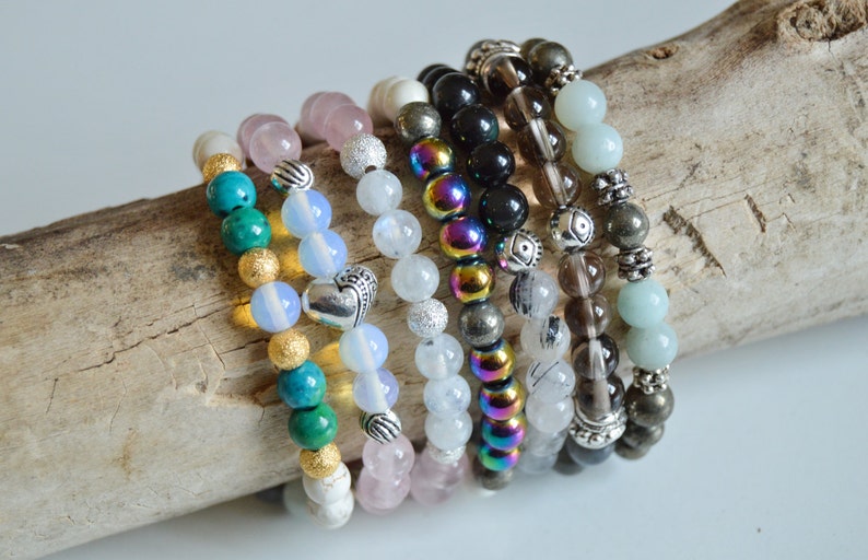 May include: A stack of eight beaded bracelets in various colors, including turquoise, pink, white, black, brown, and green. The bracelets are made with different types of beads, including gemstone beads, metal beads, and glass beads.