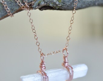 May include: A rose gold chain necklace with a white selenite crystal pendant. The crystal is wrapped in rose gold wire and hangs from the chain.