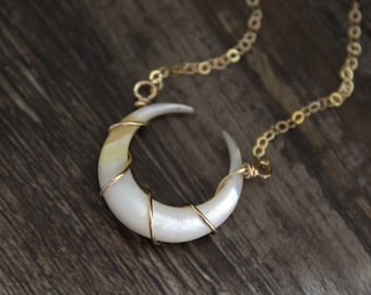 May include: A crescent moon pendant crafted from iridescent white shell, secured with thin gold-toned wire wrapping. The pendant is suspended from a delicate gold-toned metal chain with circular links, creating a simple and elegant necklace design.