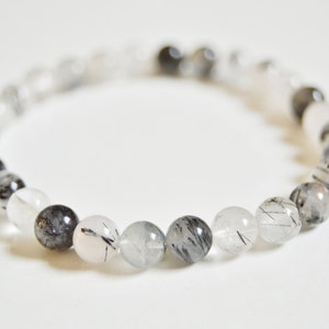 May include: A bracelet made of clear and black quartz beads. The beads are round and have a smooth, polished finish. The bracelet is approximately 7 inches in length.
