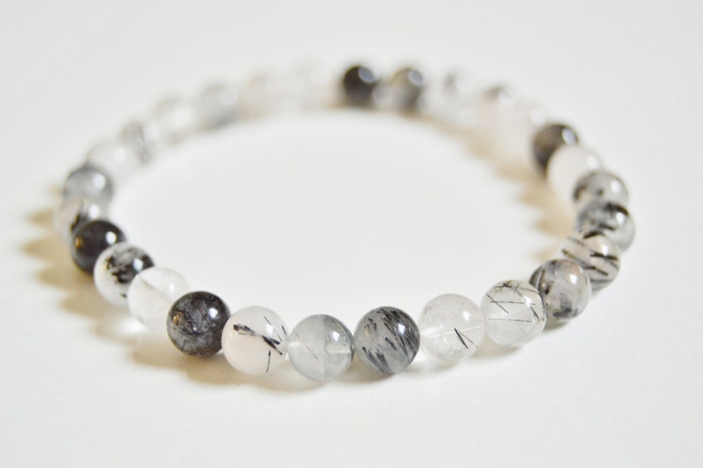 May include: A bracelet made of clear and black quartz beads. The beads are round and have a smooth, polished finish. The bracelet is approximately 7 inches in length.