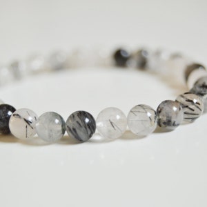 May include: A bracelet made of clear quartz beads with black tourmaline inclusions. The beads are round and have a smooth, polished finish.