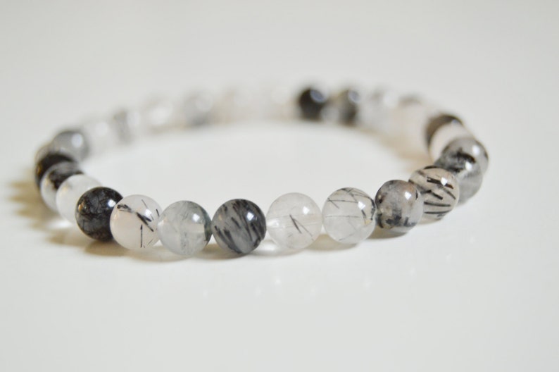May include: A bracelet made of clear quartz beads with black tourmaline inclusions. The beads are round and have a smooth, polished finish.