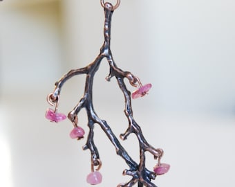 May include: A copper necklace with a delicate branch pendant adorned with pink gemstones. The branch is intricately detailed and the gemstones are set in a cluster.