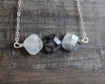 May include: A silver chain necklace with three faceted gemstone beads. The beads are clear quartz with black inclusions, and the center bead is darker than the two on either side.