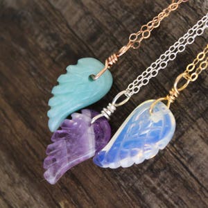 May include: Three necklaces with angel wing pendants made of different stones. The top necklace has a light blue pendant, the middle necklace has a purple pendant, and the bottom necklace has a white pendant.