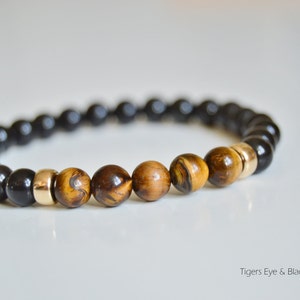 May include: A beaded bracelet featuring black obsidian and tiger's eye stones, separated by gold spacers.  Tigers Eye & Black Obsidian.