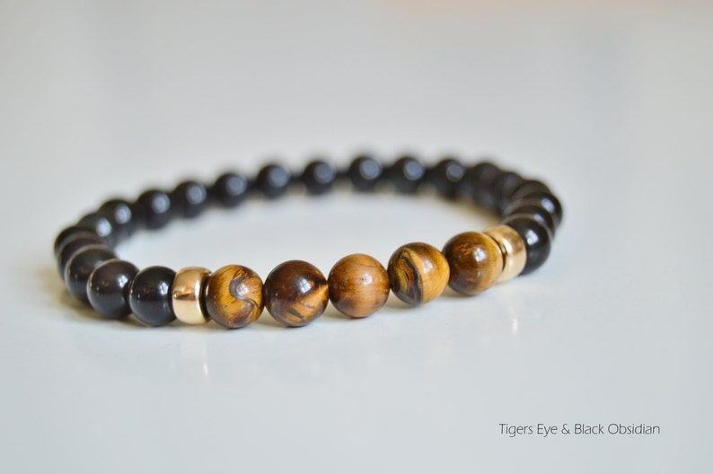 May include: A beaded bracelet featuring black obsidian and tiger's eye stones, separated by gold spacers.  Tigers Eye & Black Obsidian.