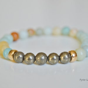 May include: A bracelet made with amazonite and pyrite beads. The bracelet has a gold accent.