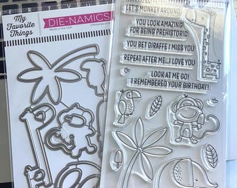 May include: A set of My Favorite Things clear stamps and matching metal dies featuring safari animal illustrations including a giraffe, monkey, elephant, crocodile, and toucan, with phrases like LET'S MONKEY AROUND and YOU LOOK AMAZING FOR BEING PREHISTORIC.