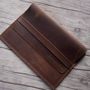 Peut inclure: Une pochette pour ordinateur portable en cuir marron avec une fermeture &agrave; rabat et une inscription personnalis&eacute;e qui dit "Zachary K. Choi".