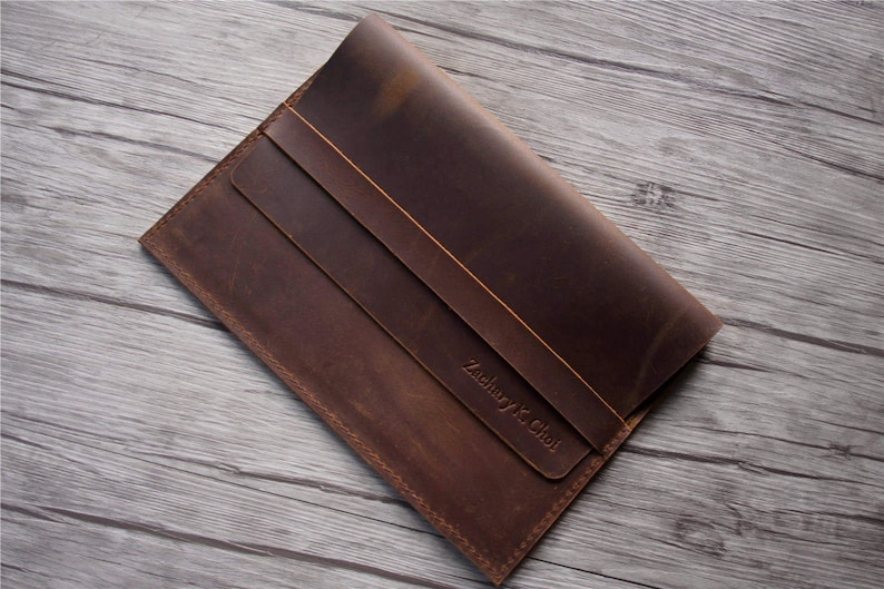 Peut inclure: Une pochette pour ordinateur portable en cuir marron avec une fermeture &agrave; rabat et une inscription personnalis&eacute;e qui dit "Zachary K. Choi".