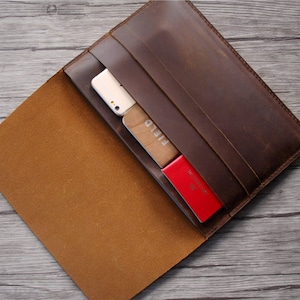 Peut inclure: Un porte-documents en cuir marron avec une fermeture &agrave; rabat. Le porte-documents est ouvert et contient un t&eacute;l&eacute;phone, des cartes et un passeport.