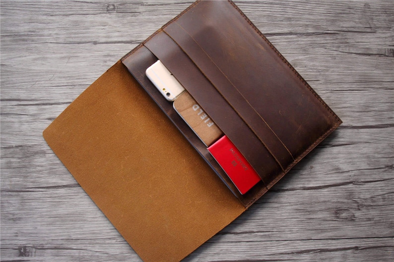 Peut inclure: Un porte-documents en cuir marron avec une fermeture &agrave; rabat. Le porte-documents est ouvert et contient un t&eacute;l&eacute;phone, des cartes et un passeport.