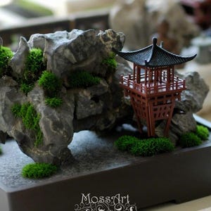 Peut inclure: Un jardin miniature de bonsaï avec une formation rocheuse grise, de la mousse verte vibrante et une petite pagode rouge. La scène est présentée dans un pot rectangulaire brun foncé, créant une esthétique sereine et naturelle.