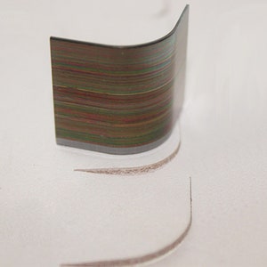 May include: A close-up of a curved, metallic ruler with a rainbow-like pattern of colored lines. The ruler is resting on a white surface, leaving a faint, curved line in the surface.