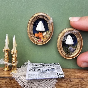 Puede incluir: Miniaturas temáticas de Halloween. Dos marcos ovalados con figuras de fantasmas y decoración otoñal. Un pequeño periódico con el titular "EXTRA! EXTRA!" descansa sobre un paño de arpillera, junto a dos candelabros dorados.