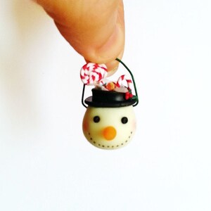 May include: A small snowman ornament with a black top hat, red and white candy cane, and green wire loop for hanging.
