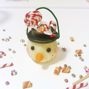 May include: A small snowman figurine with a black hat and a candy cane and lollipop in the hat. The snowman is surrounded by small candy canes and lollipops.