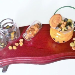 May include: A miniature wooden table with a pumpkin-shaped candy bucket, three glass jars filled with candy, and loose candy scattered on the table. The candy is a mix of orange and black.