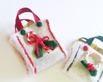 May include: Two white felt Christmas gift bags with red and green trim. One bag has a candy cane and holly, the other has a wreath and holly.