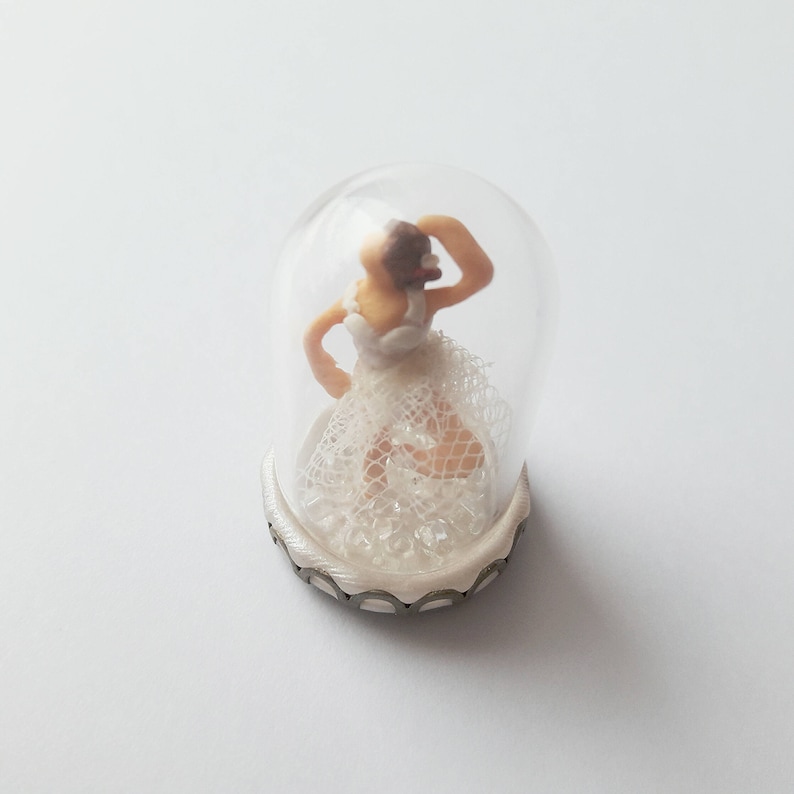 May include: A miniature ballerina figurine wearing a white lace dress is encased in a clear glass dome with a silver base.