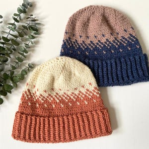 Puede incluir: Dos gorros de invierno de ganchillo con patrones de color degradado. El gorro de arriba es rosa y azul, y el gorro de abajo es crema y naranja.