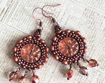 May include: Copper-toned beaded earrings with a central faceted gem and dangling beads. The earrings have a circular design with a detailed beaded border and a decorative hook.
