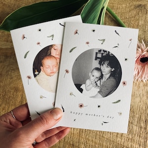 May include: Two white Mother's Day cards with black and white photos of a mother and child. The cards are decorated with small floral and leaf illustrations. The phrase "happy mother's day" is printed on the bottom of the cards.