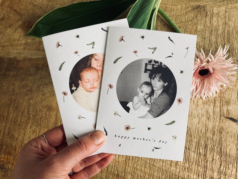 May include: Two white Mother's Day cards with black and white photos of a mother and child. The cards are decorated with small floral and leaf illustrations. The phrase "happy mother's day" is printed on the bottom of the cards.