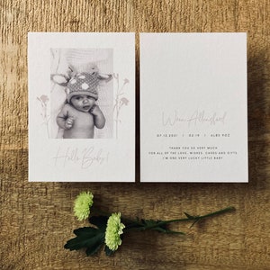 Op de afbeelding: Een witte kaart met een foto van een baby die een gestippelde hoed draagt en de tekst "Hello Baby!" op de voorkant. De achterkant van de kaart heeft de tekst "Wren Allengford 07.12.2021 | 03:19 | 6lbs 9oz Hartelijk dank voor al de liefde, wensen, kaarten en cadeaus. Ik ben een heel gelukkig klein babytje."