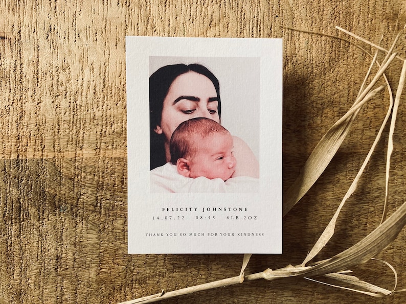 May include: A newborn baby girl is being held by her mother. The baby is wearing a white onesie and the mother is wearing a white shirt. The image is in a soft, warm tone. The text on the card reads "Felicity Johnstone 14.07.22 08:45 6LB 2OZ Thank you so much for your kindness."