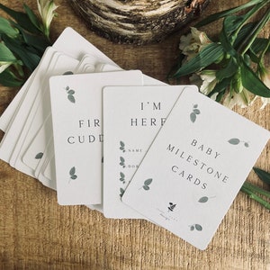 Pode incluir: Um conjunto de cart&otilde;es de marcos para beb&ecirc;s com um design simples que inclui folhas verdes e o texto "Baby Milestone Cards".