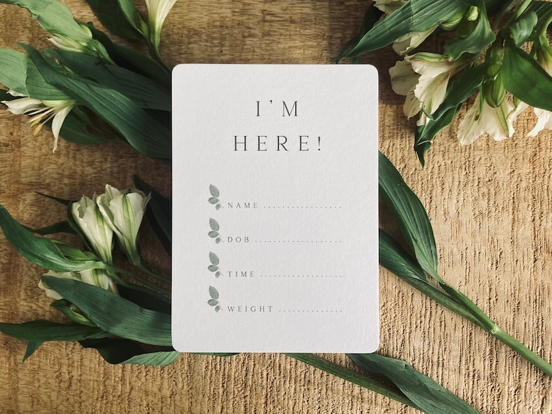 Pode incluir: Um cart&atilde;o branco com o texto "I'M HERE!" e uma lista de informa&ccedil;&otilde;es para preencher: nome, data de nascimento, hora e peso. O cart&atilde;o &eacute; decorado com pequenas ilustra&ccedil;&otilde;es de borboletas cinzas.