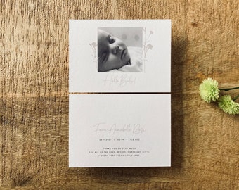 May include: A black and white photo of a newborn baby sleeping. The photo is surrounded by a floral design and the text "Hello Baby!" is written below the photo. The text "Fawn Annabelle Rose" is written in cursive below the photo, along with the date "24.11.2021" and the text "1.8lb 5oz". The text "Thank you so very much for all of the love, wishes, cards and gifts. I'm one very lucky little baby." is written below the date.