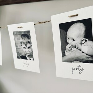 May include: Black and white photos of a baby, a young child, and a teenager, strung together on a twine line with clothespins. Each photo has the word "forty" written below it.