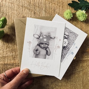 Op de afbeelding: Twee kaarten met zwart-witfoto's van baby's. De eerste kaart heeft een baby met een gestippelde hoed en de tekst "Hello Baby!" De tweede kaart heeft een baby met een gebreid outfit. Beide kaarten hebben een bloemmotief.