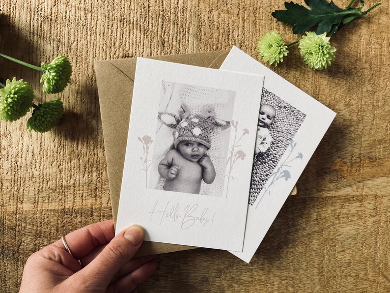 Op de afbeelding: Twee kaarten met zwart-witfoto's van baby's. De eerste kaart heeft een baby met een gestippelde hoed en de tekst "Hello Baby!" De tweede kaart heeft een baby met een gebreid outfit. Beide kaarten hebben een bloemmotief.