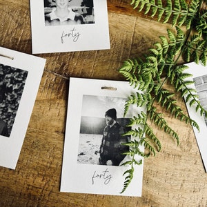 May include: A set of four black and white photos with a white border and the word "forty" written in cursive at the bottom of each photo. The photos are strung together with twine and are hanging against a wooden background.