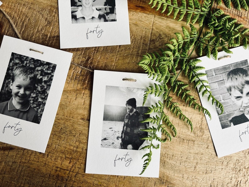 May include: A set of four black and white photos with a white border and the word "forty" written in cursive at the bottom of each photo. The photos are strung together with twine and are hanging against a wooden background.