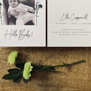 Op de afbeelding: Een witte kaart met een zwart-witfoto van een baby en de tekst "Hello Baby!"  Een tweede witte kaart met de tekst "Ella Copperwell 31.01.2022 | 19:02 | 8LBS 8OZ" en "Bedankt voor al de liefde, wensen, kaarten en cadeaus. Ik ben een heel gelukkig klein baby."