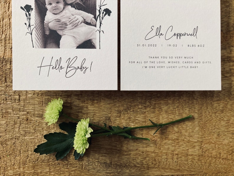 Op de afbeelding: Een witte kaart met een zwart-witfoto van een baby en de tekst "Hello Baby!"  Een tweede witte kaart met de tekst "Ella Copperwell 31.01.2022 | 19:02 | 8LBS 8OZ" en "Bedankt voor al de liefde, wensen, kaarten en cadeaus. Ik ben een heel gelukkig klein baby."