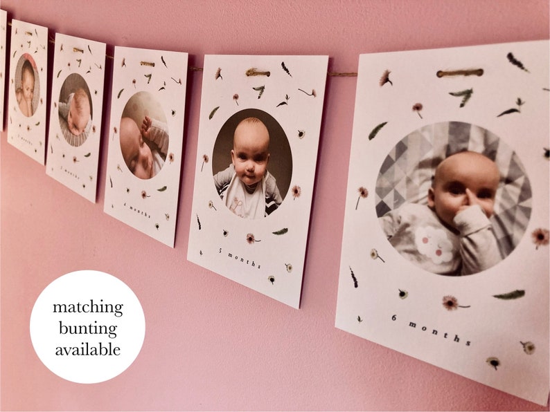 May include: A set of white photo cards with a circular cutout for a photo of a baby. Each card has a floral design and the text "x months" printed on it. The cards are strung together with twine.